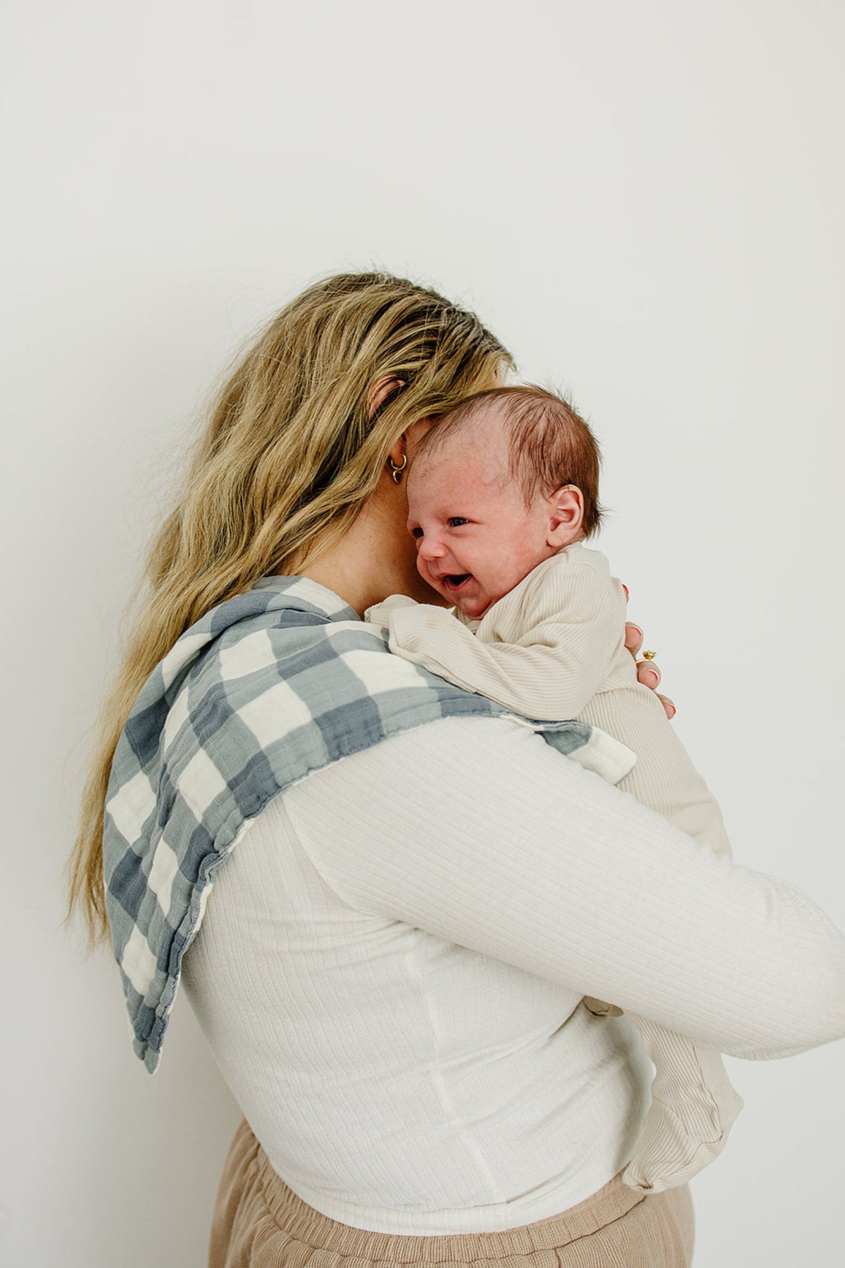 A woman holds a baby on her shoulder with a dusty blue gingham muslin burp cloth draped over it.