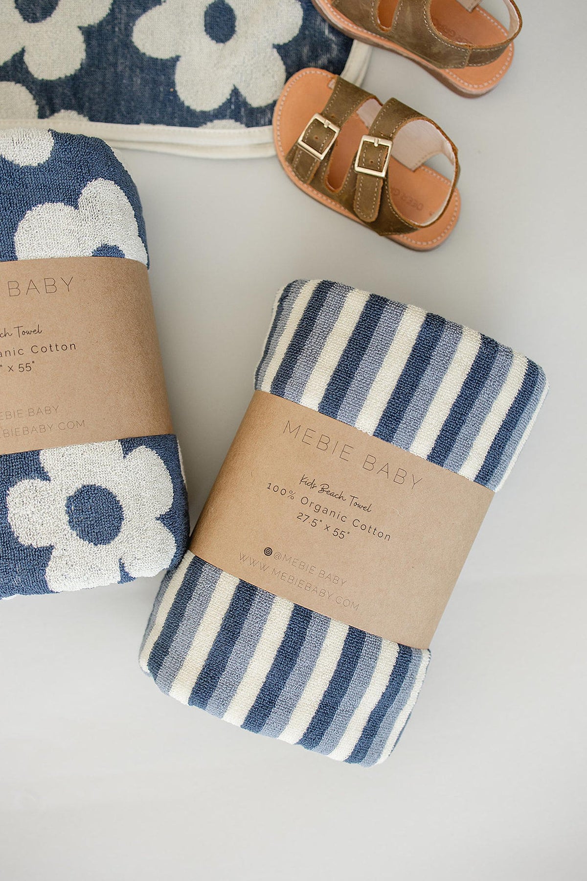 Navy and white striped organic cotton beach towel with floral pattern, paired with brown toddler sandals on a light background.