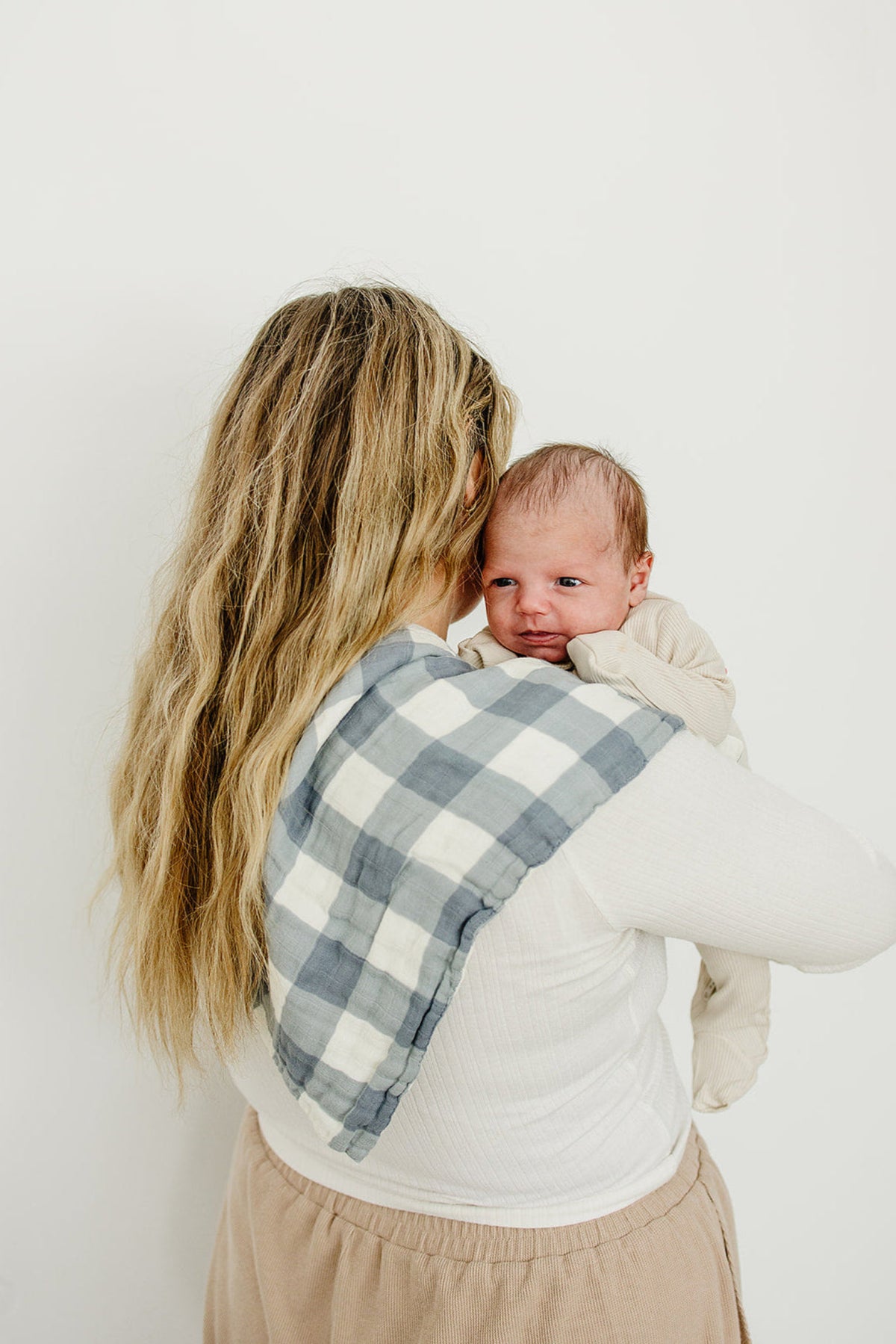 A woman holds a baby with a dusty blue gingham muslin burp cloth on her shoulder.
