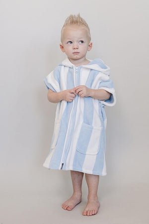 A young child stands barefoot, wearing a light blue and white striped zip-up poncho made from soft organic cotton.
