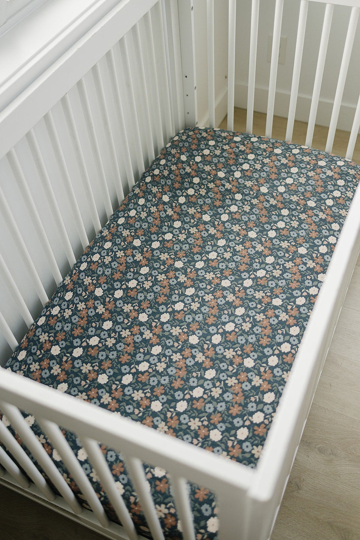 A floral muslin crib sheet in navy blue with white and orange flowers is fitted snugly over a standard crib mattress.