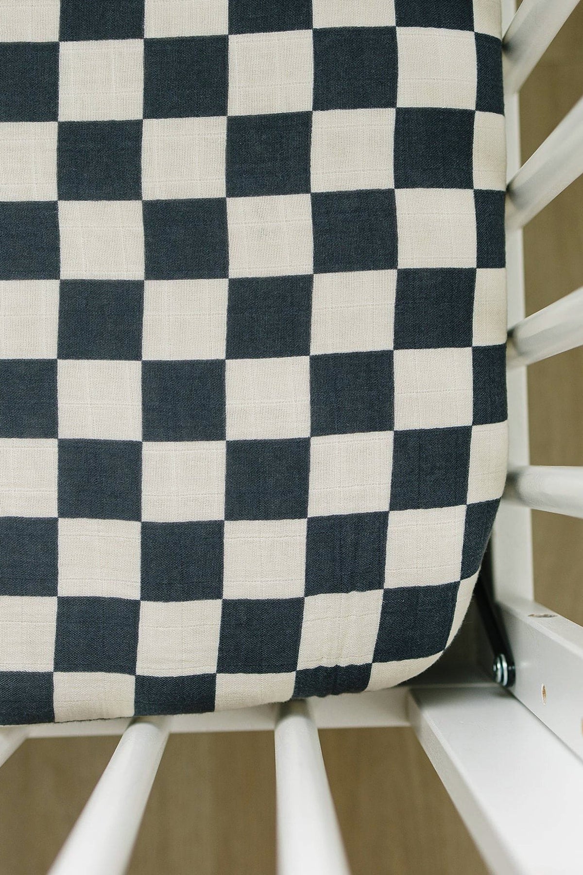 Checkered crib sheet in charcoal and white muslin fabric on a white crib. Soft, breathable, and stylish.