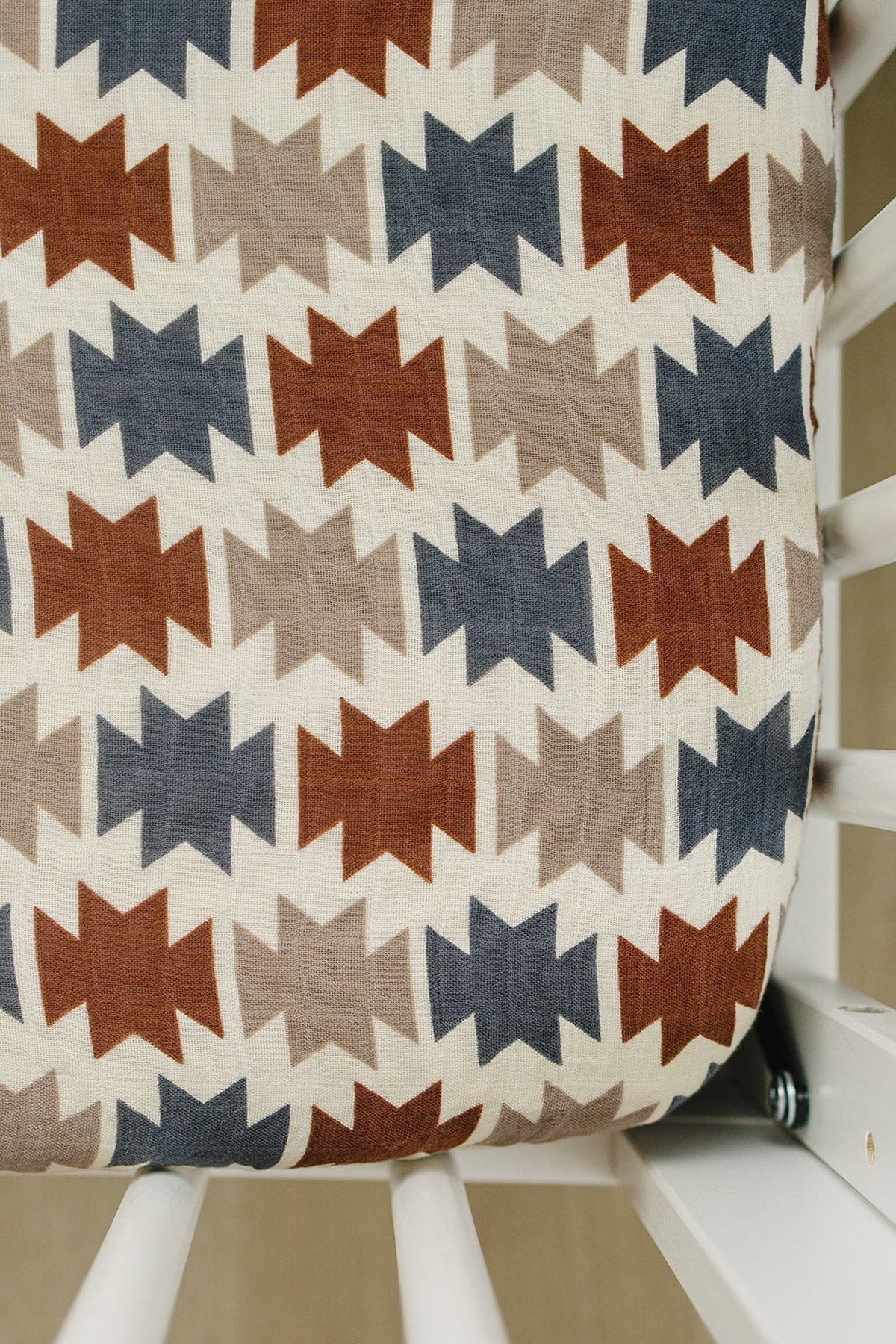 A close-up of a crib sheet featuring a Western Aztec pattern in earthy tones of red, blue, and beige.