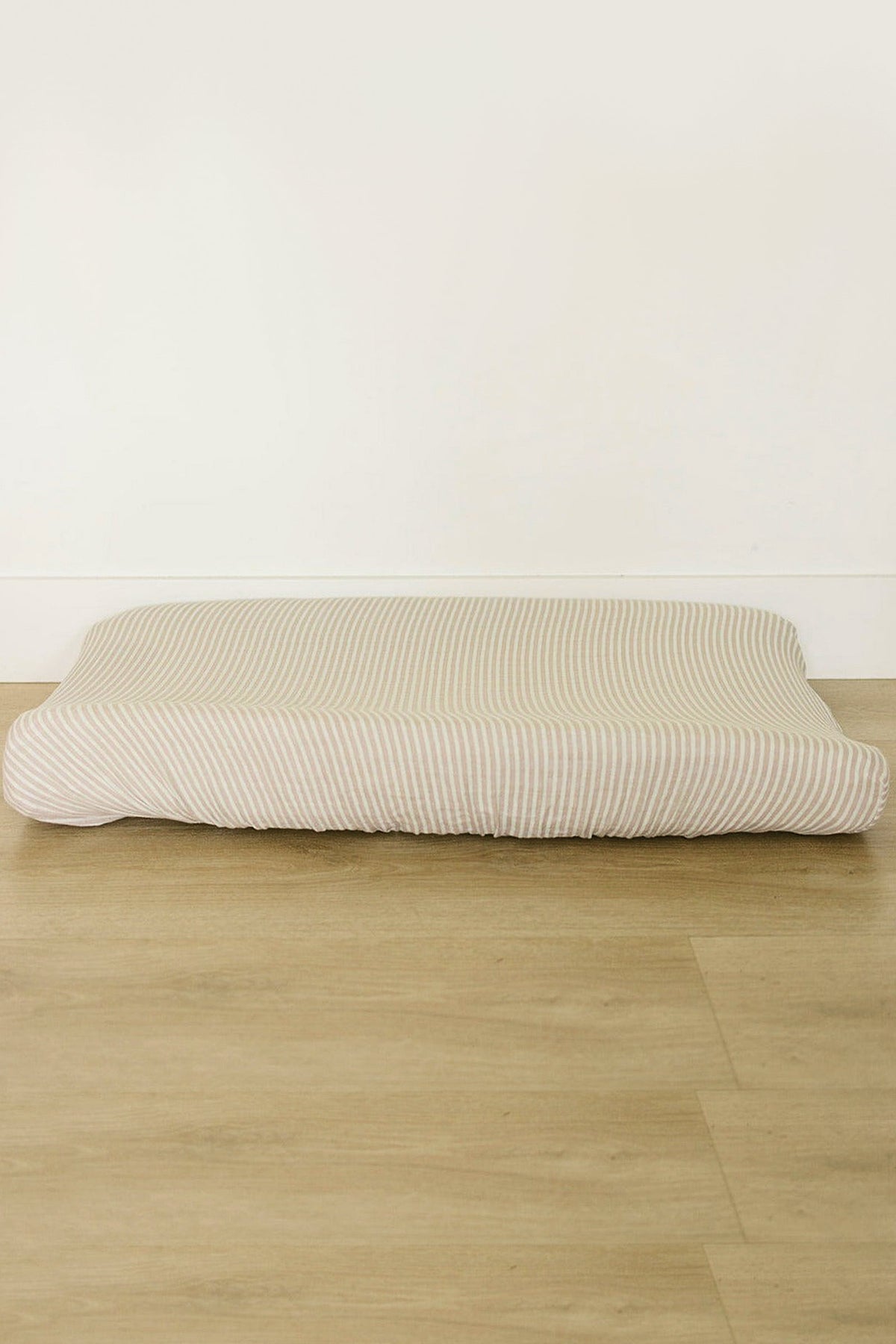Taupe striped muslin changing pad cover on a wooden floor, showcasing soft, breathable cotton fabric.