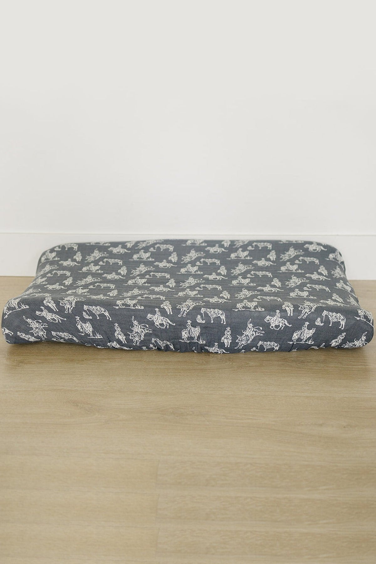 A navy blue muslin changing pad cover with white Wild West designs on a wooden floor.