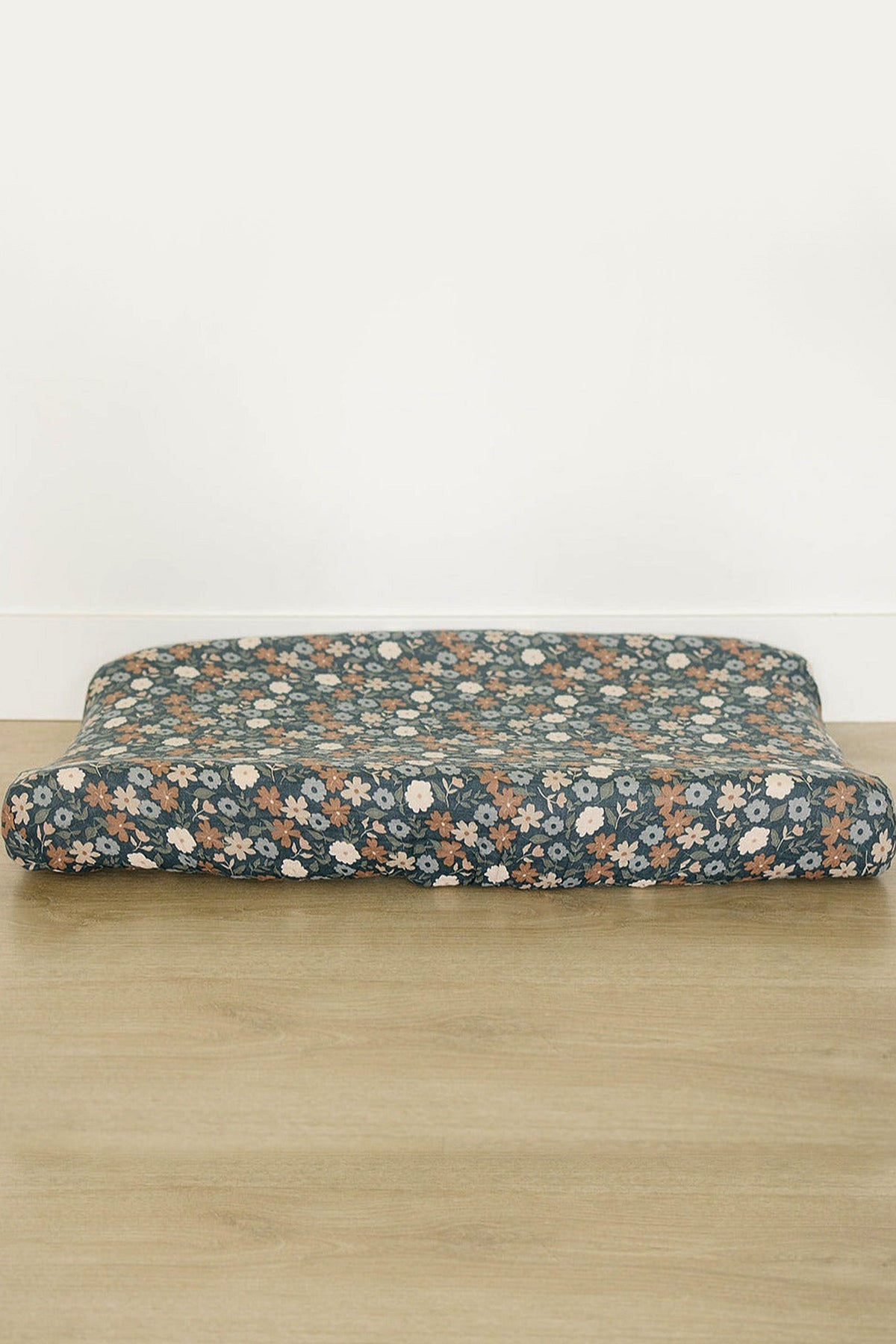 A soft muslin changing pad cover features a midnight floral print with white and orange flowers against a dark blue background.