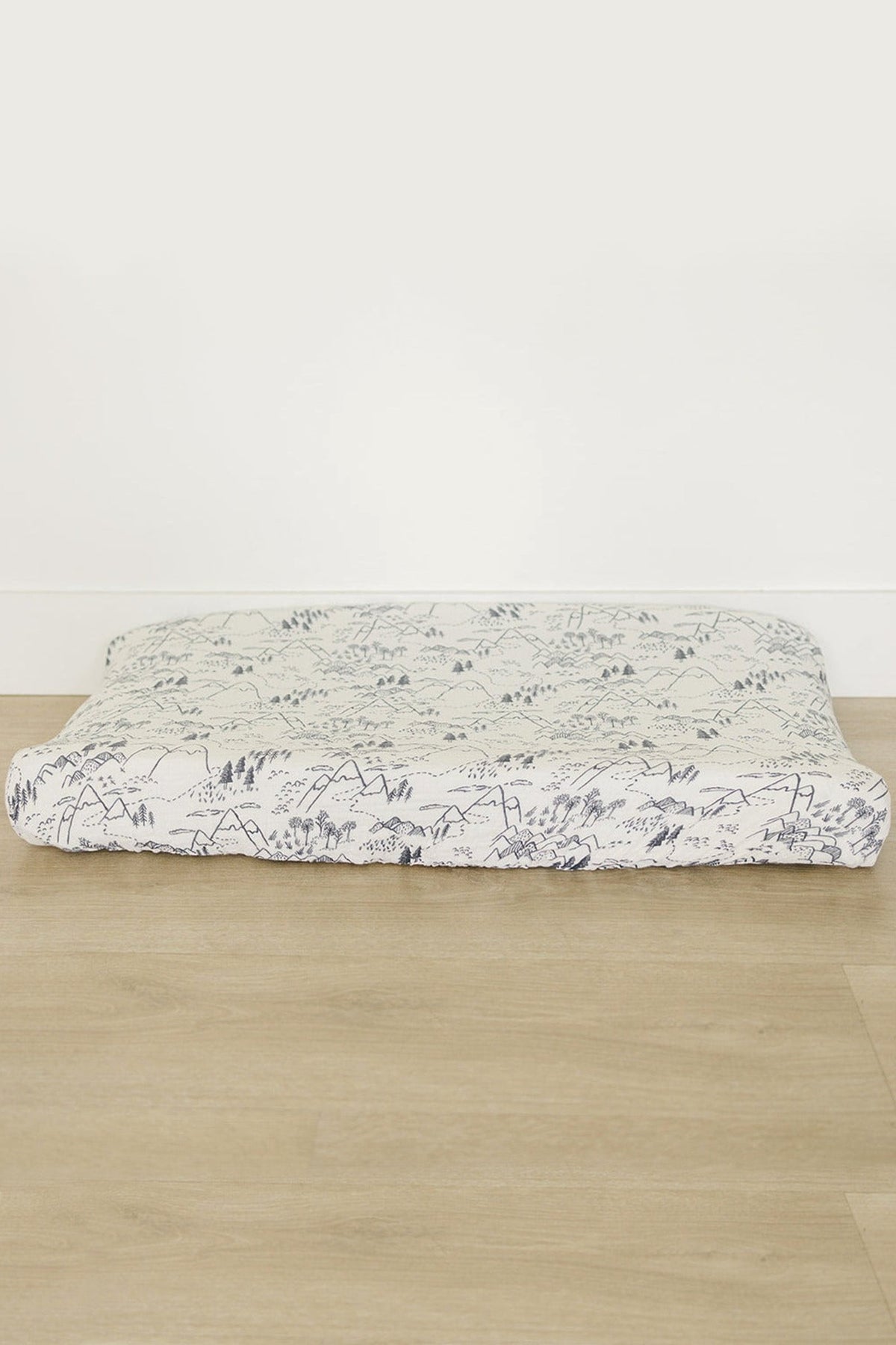 A soft muslin changing pad cover featuring a delicate mountain and forest pattern in muted colors, designed to fit standard changing pads. Ideal for creating a charming nursery decor.