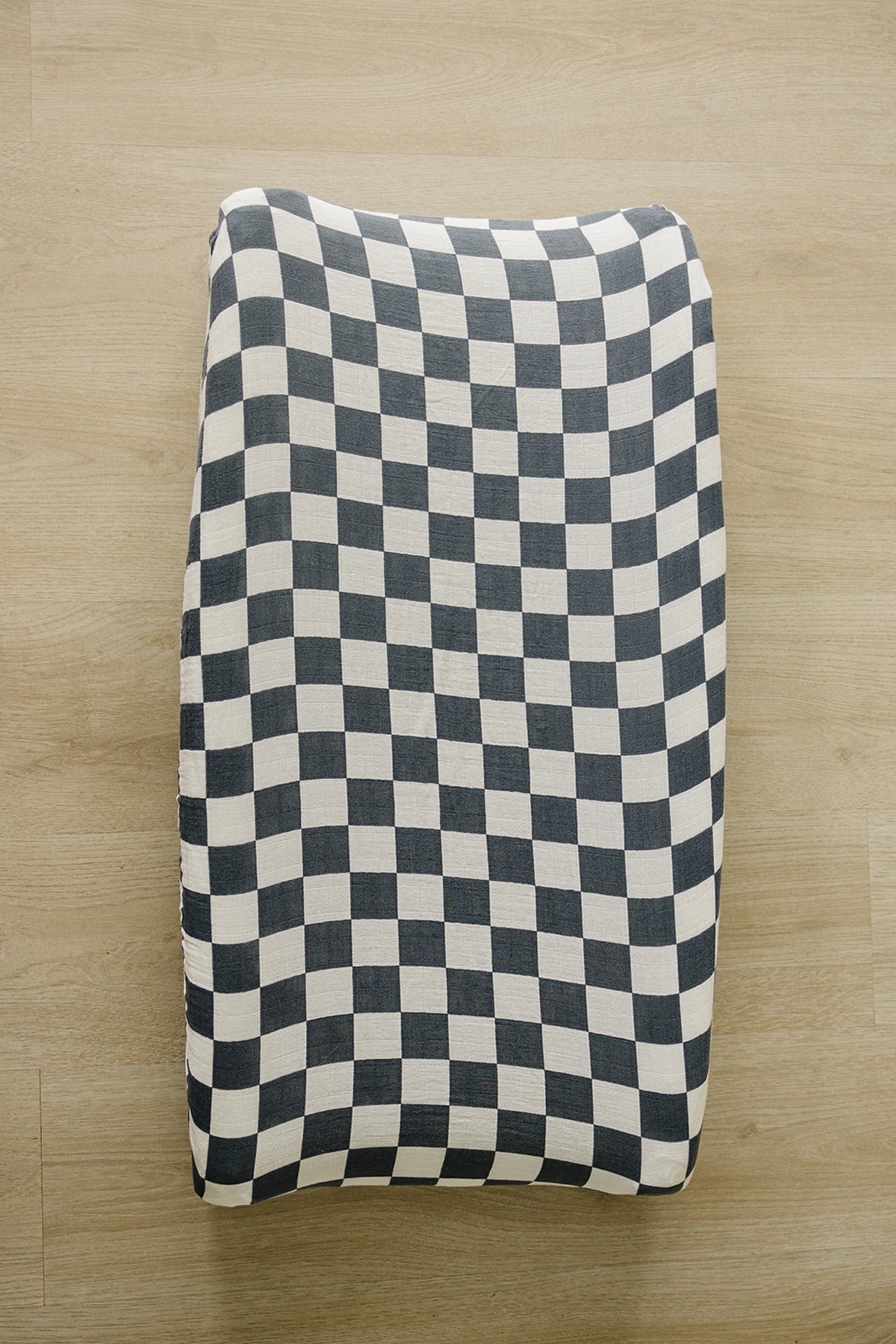 Charcoal checkered muslin changing pad cover on a wooden surface, featuring a modern and snug design.