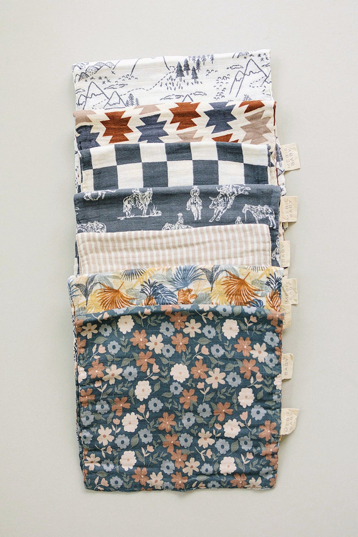 A stack of colorful muslin burp cloths featuring various patterns, including floral, geometric, and Western designs. Made from soft, breathable cotton, these cloths are ideal for baby feeding and burping.