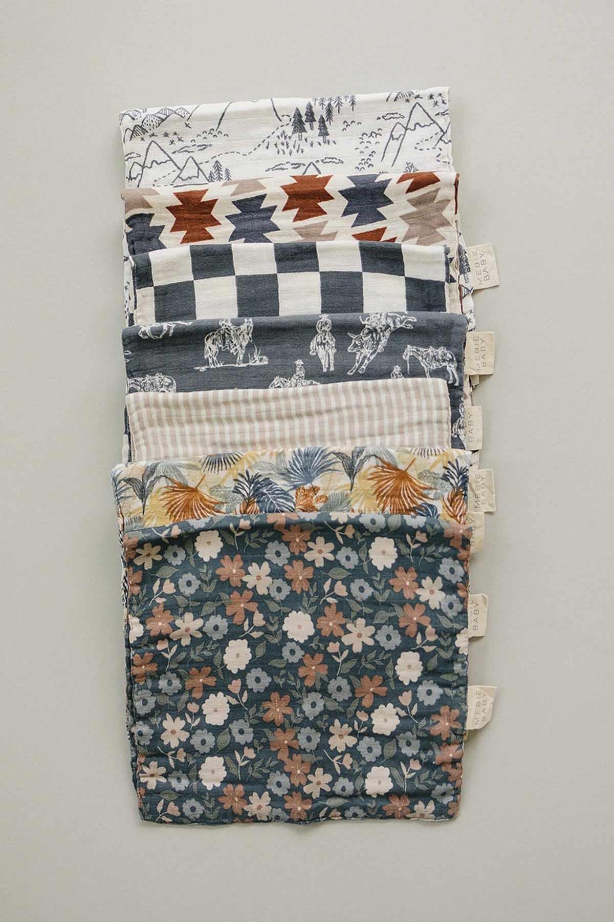 Assorted Mebie Baby muslin burp cloths with various patterns, including florals and geometric designs, stacked neatly.
