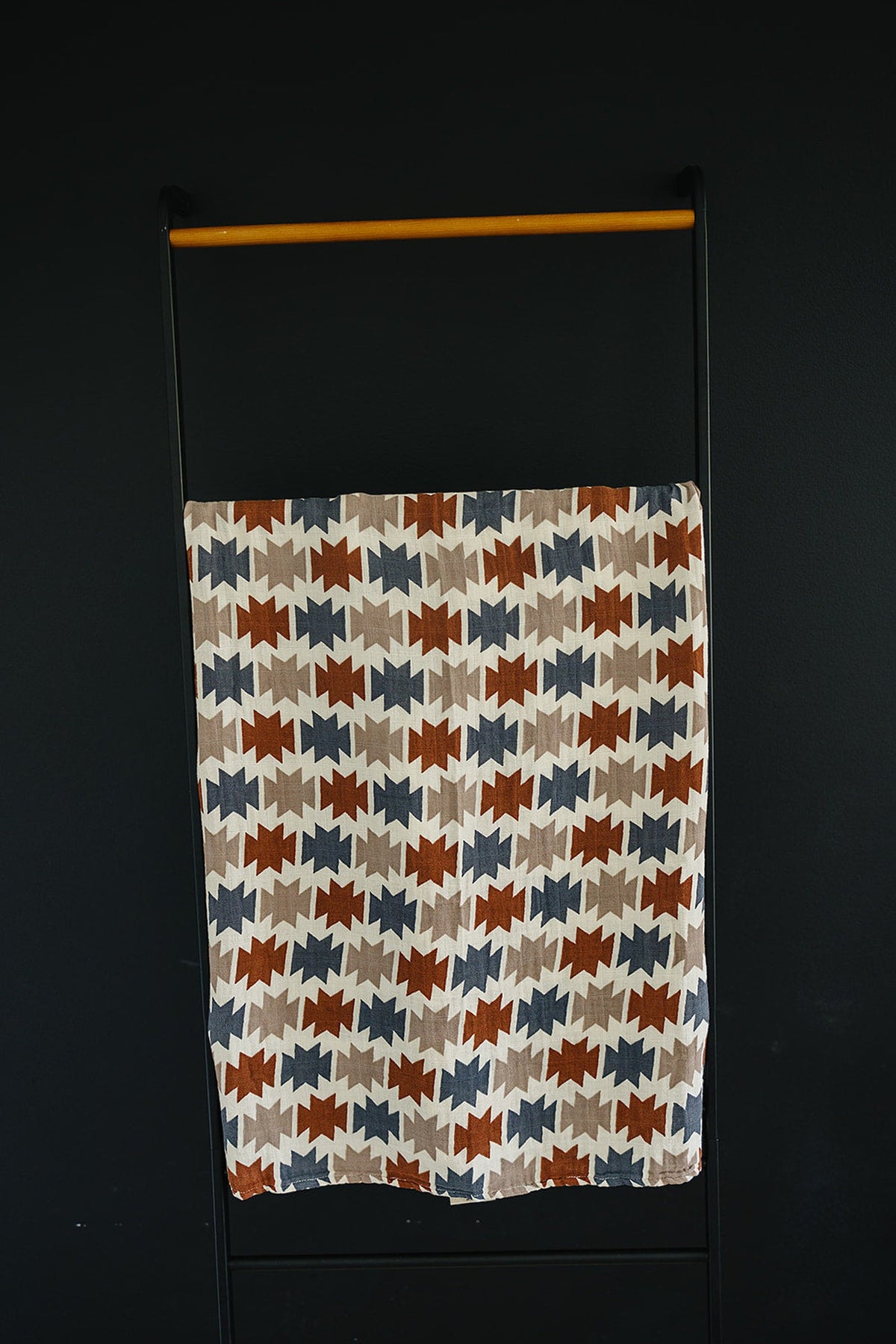 A colorful muslin blanket featuring a Western Aztec pattern in rust, blue, and beige, displayed on a black backdrop.