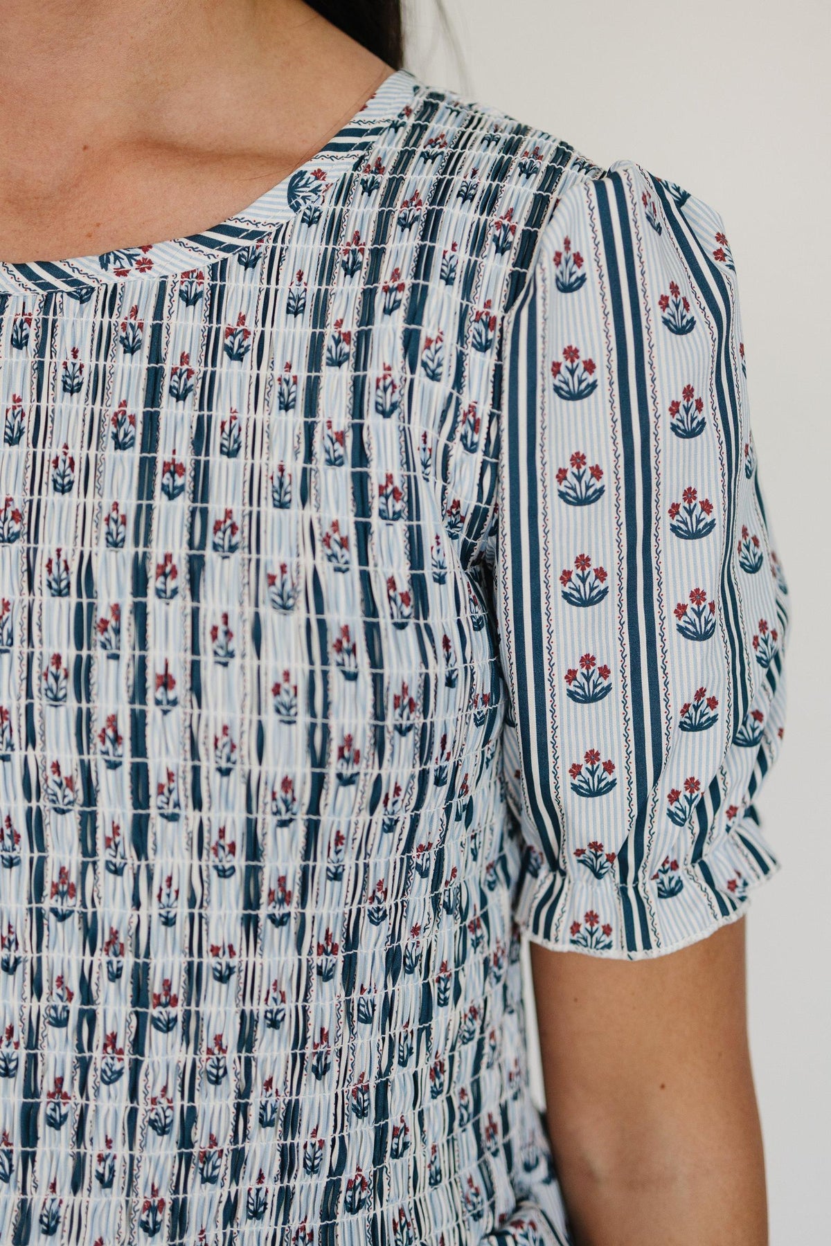 A close-up of a womans upper body wearing a cotton dress featuring a blue and white floral block print.
