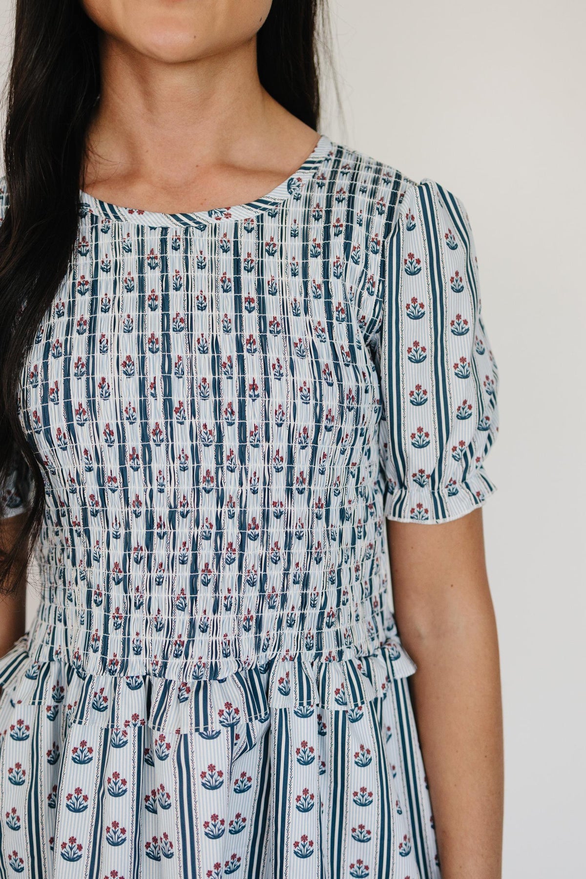 A close-up of a woman wearing a floral block print dress featuring a smocked bodice and puff sleeves.