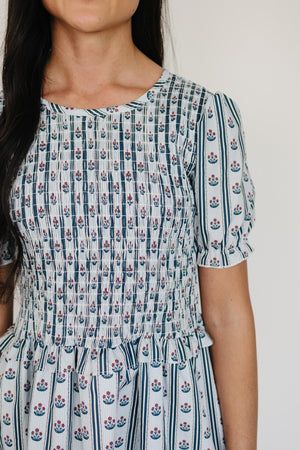 A close-up of a woman wearing a floral block print dress featuring a smocked bodice and puff sleeves.