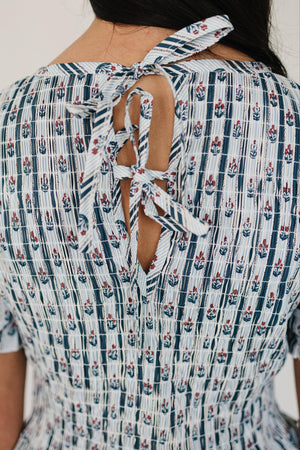 Back view of a floral block print dress featuring a tie closure, crafted from breathable cotton. The design showcases a delicate pattern in soft colors, perfect for casual outings.