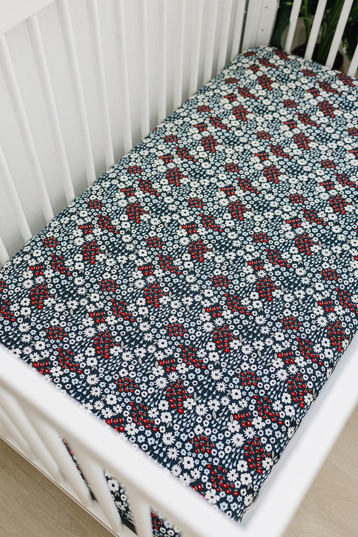 White crib with a navy crib sheet featuring red and white floral patterns, made from soft bamboo fabric.