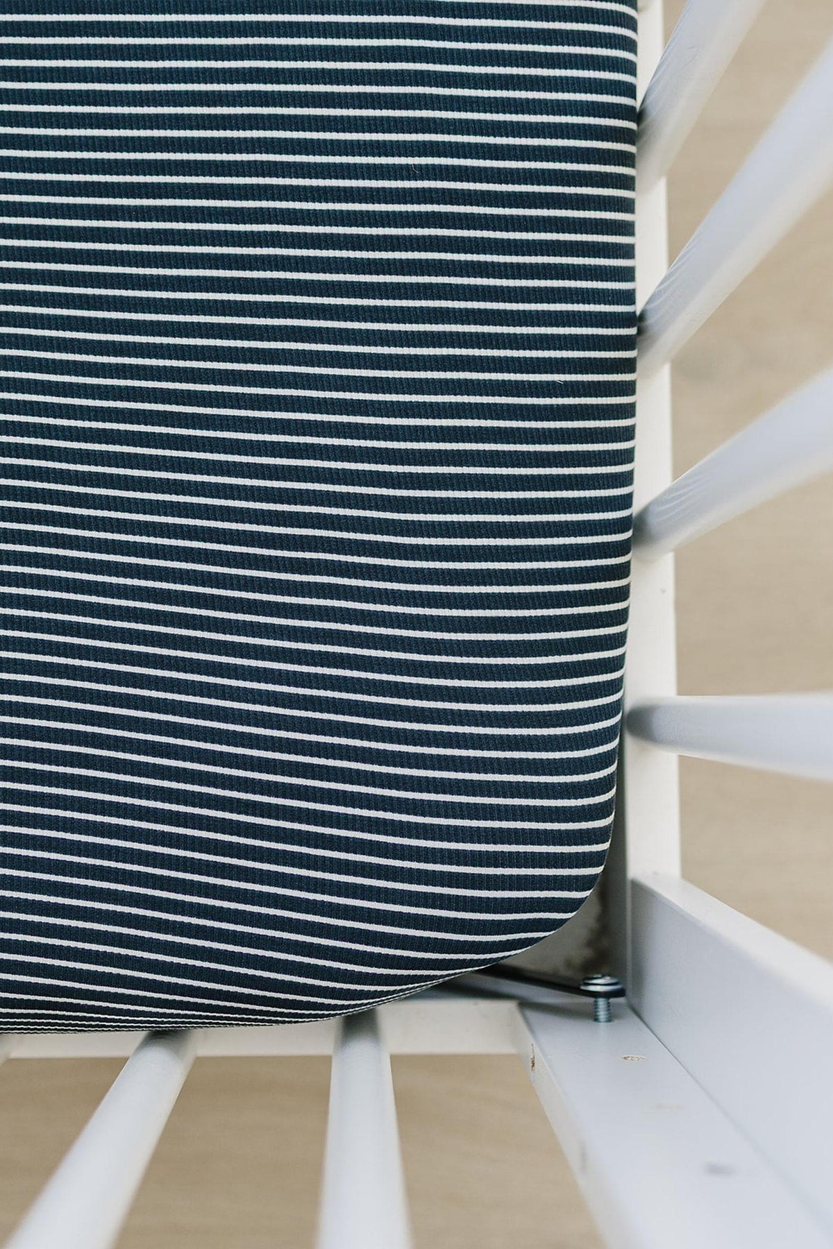Navy and white striped crib sheet on a white crib corner, showcasing a soft, breathable fabric.