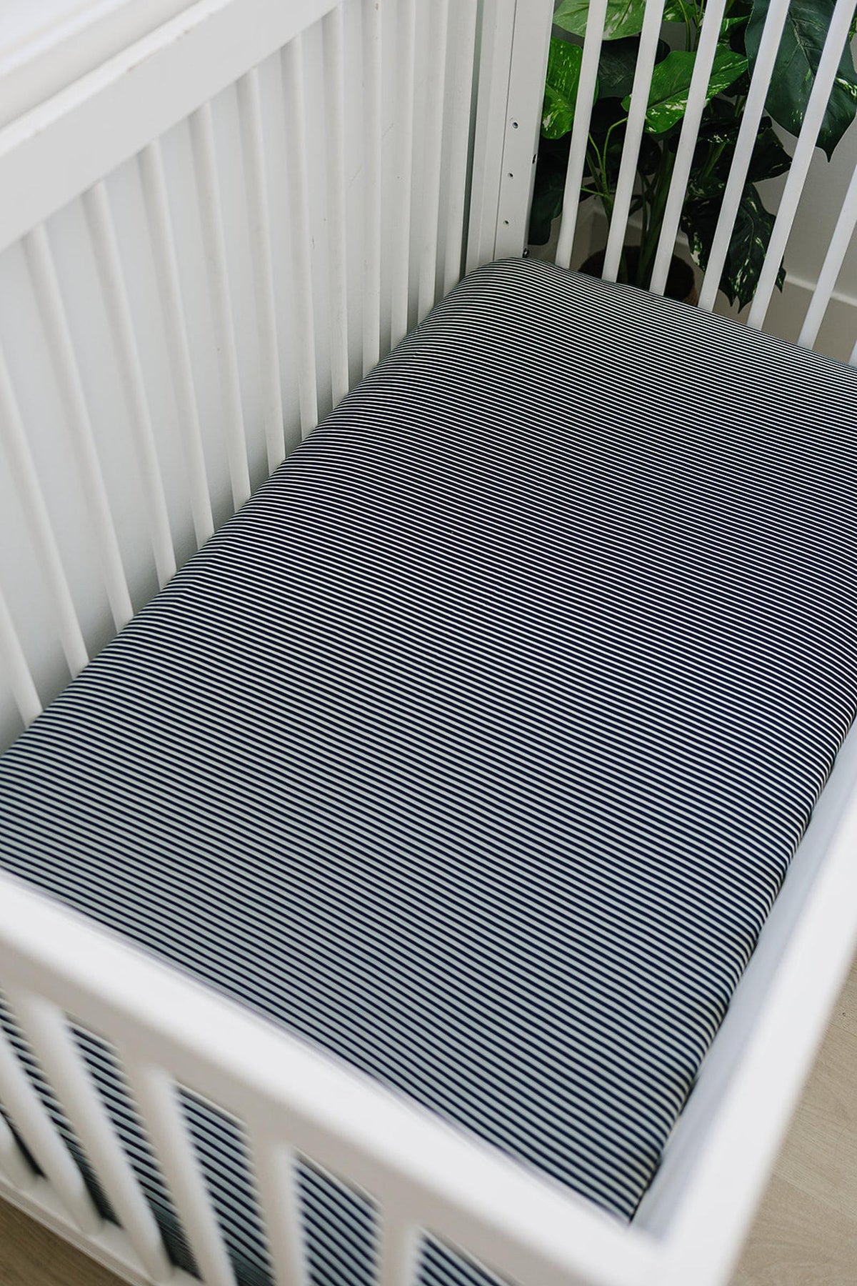 White crib with a navy striped crib sheet, made from soft bamboo fabric, in a nursery setting.