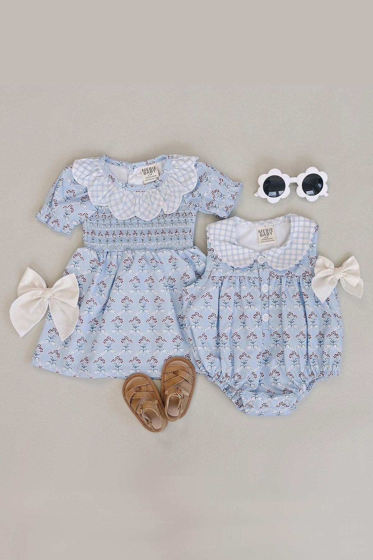 A light blue baby dress and matching romper feature a charming gingham collar and delicate floral patterns. Accompanied by stylish accessories, they are perfect for playful adventures.