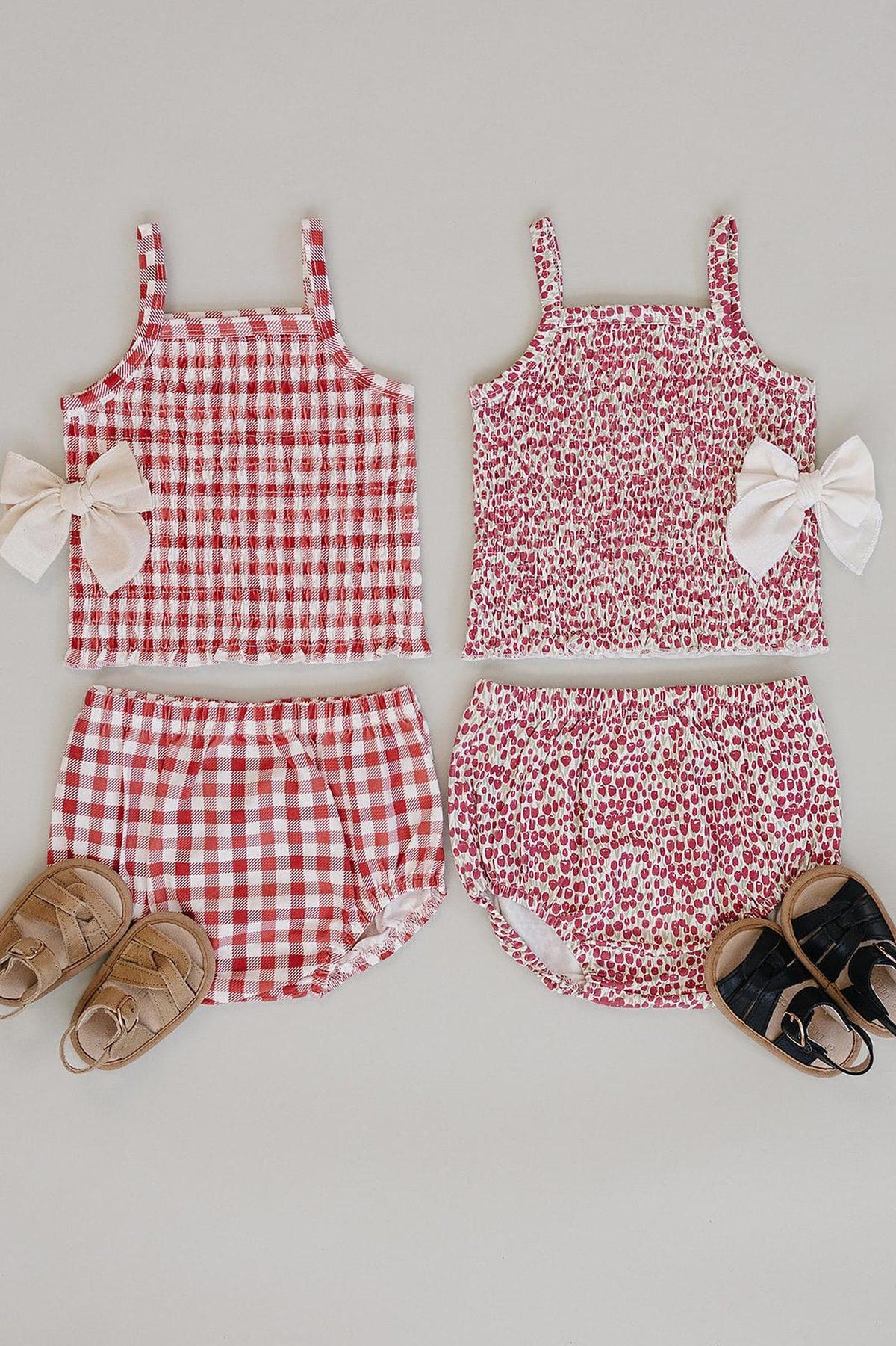 Two baby girl outfits displayed flat: a red gingham top and bloomer set, and a floral print top with matching.