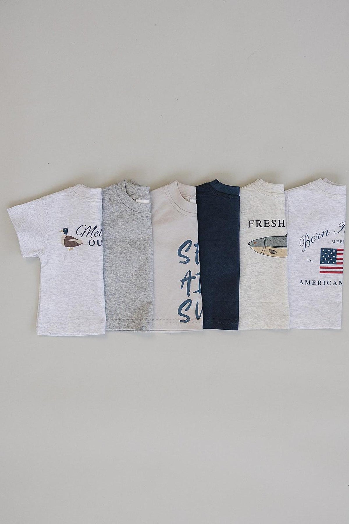 Six cotton t-shirts in various colors and designs, including graphics and text, displayed on a neutral background.