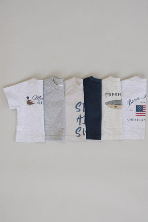 A display of five cotton t-shirts in various colors, featuring playful graphics like “Sea Air Sun” and a duck motif.