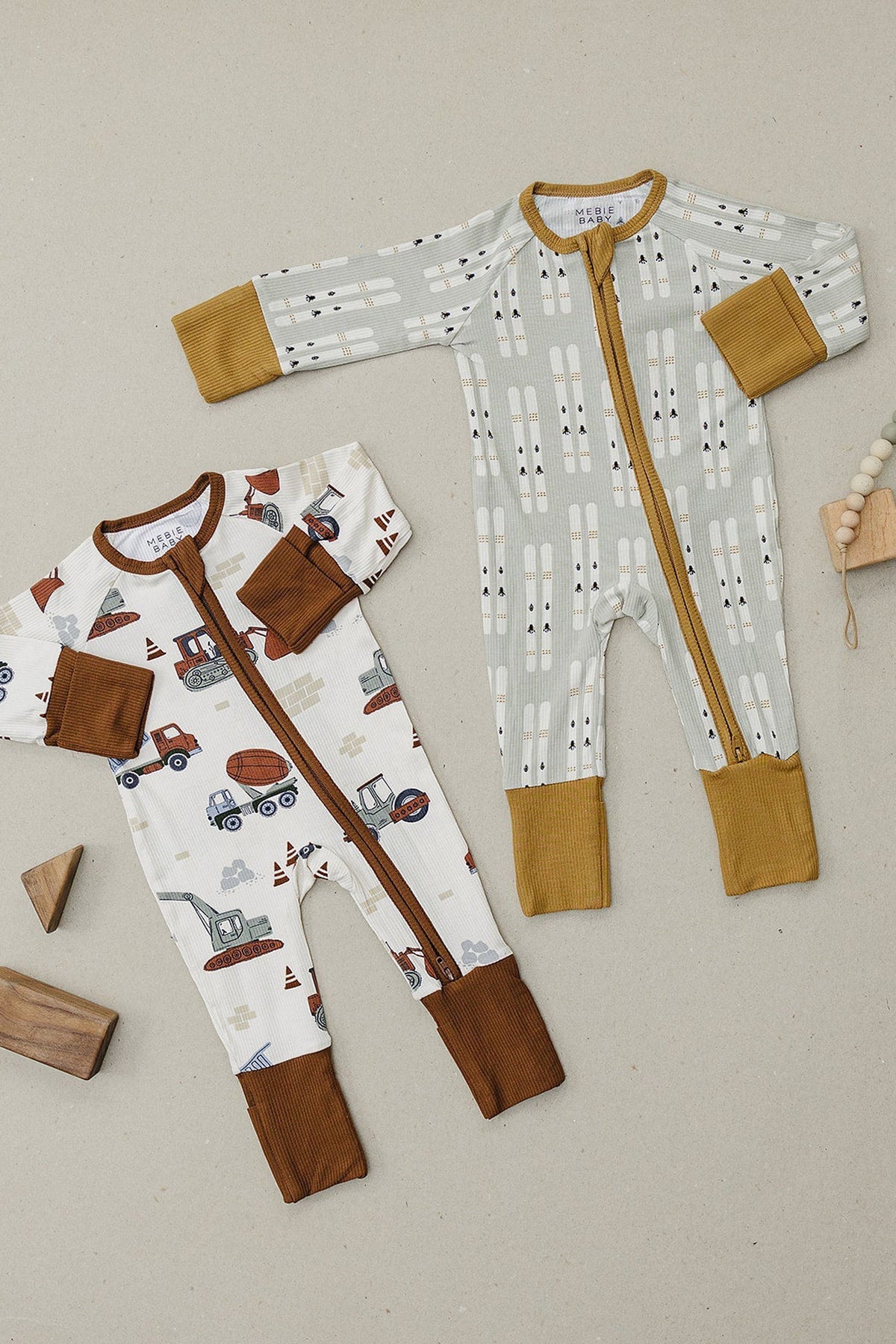 Two Mebie Baby zippered pajamas with ski and vehicle patterns, featuring ribbed cuffs and eco-friendly bamboo fabric.