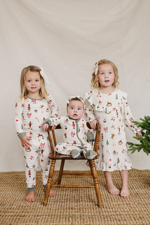 Three children are styled in festive holiday pajamas featuring cheerful prints on soft, organic bamboo fabric. They stand together in front of a neutral backdrop, exuding a cozy, cheerful vibe.