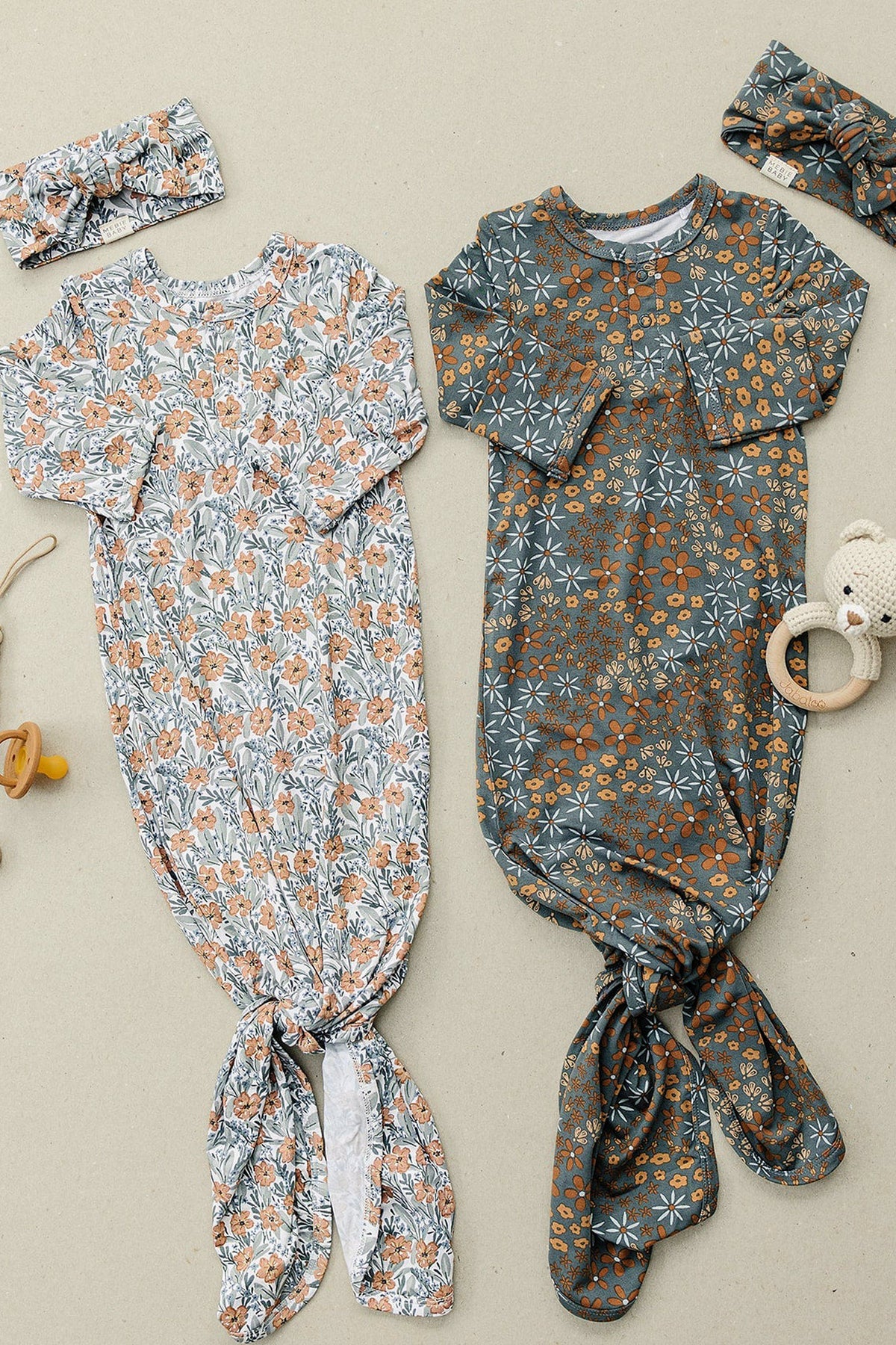 Two floral baby gowns with matching headbands on a beige background, featuring orange and blue floral patterns.