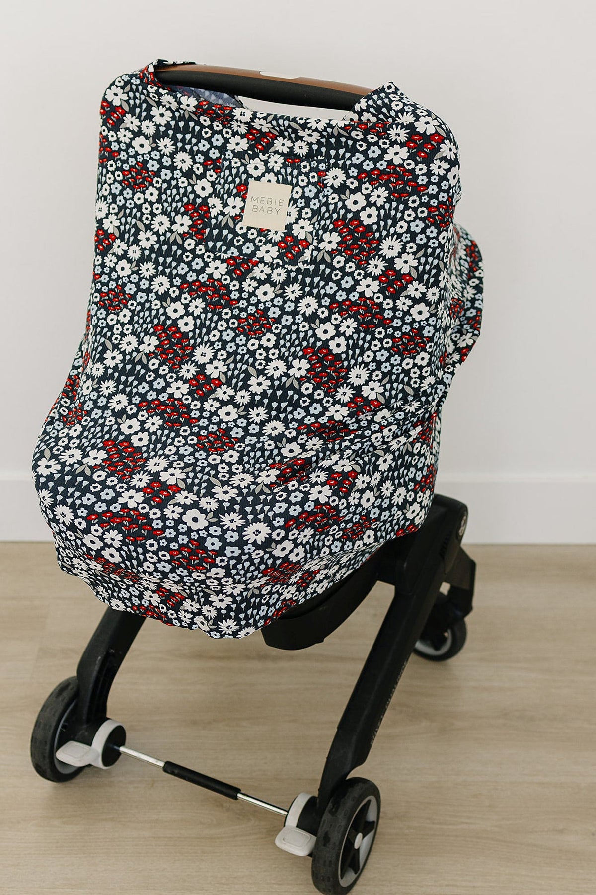 Floral-patterned Mebie Baby cover in navy, red, and white on a black stroller with wooden floor background.