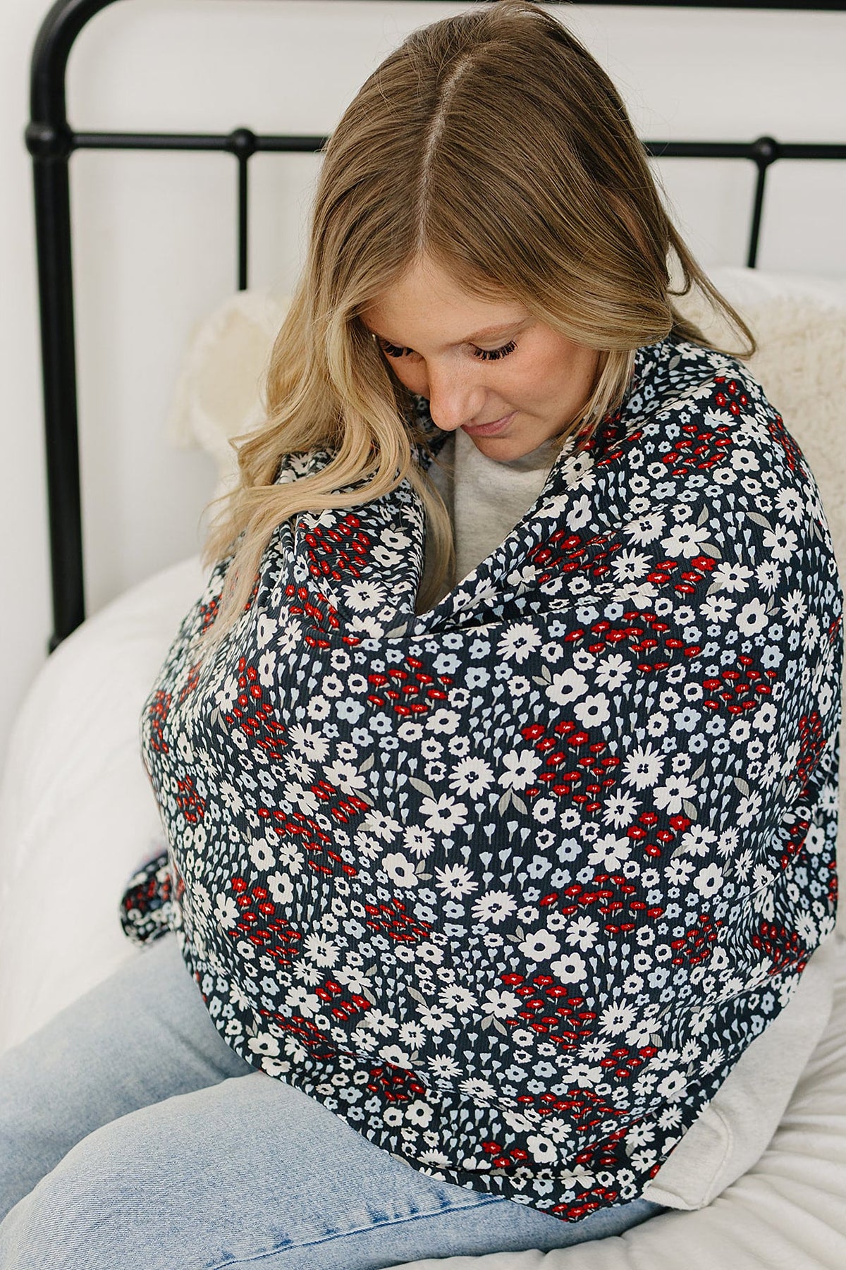 A woman sits on a bed using a floral patterned cover with red and white flowers.