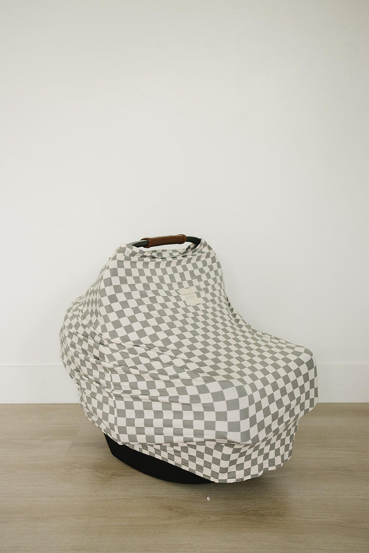 Checkered car seat cover in light green and white, draped over a baby seat on a wooden floor.
