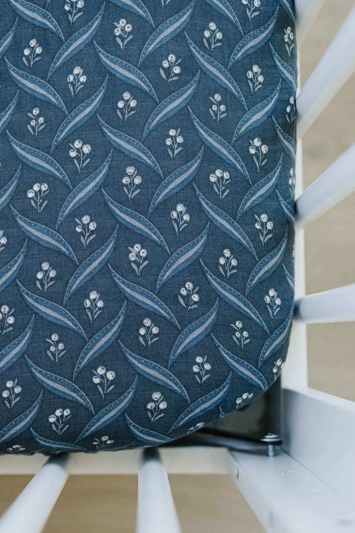 Navy crib sheet with white berry and leaf pattern on a fitted muslin fabric, set in a white crib.