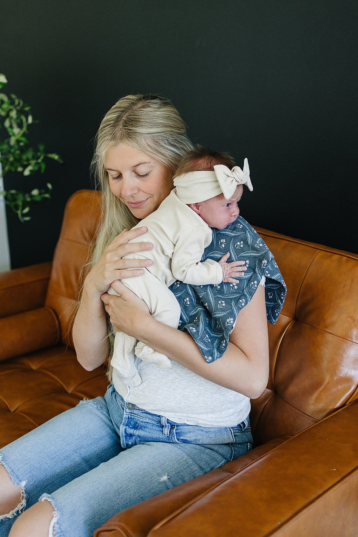 A woman holds a baby with a navy muslin burp cloth featuring a floral pattern on a leather couch.