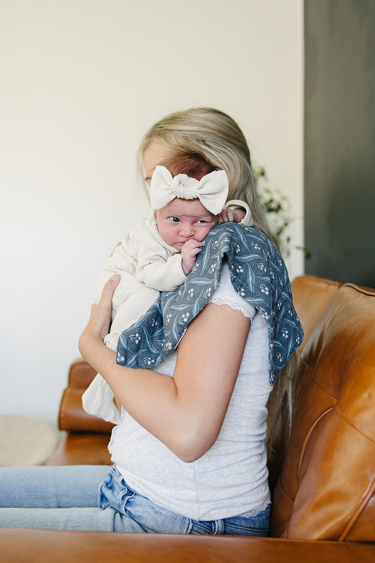 A baby with a large bow headband rests on a womans shoulder, using a blue patterned muslin burp cloth.