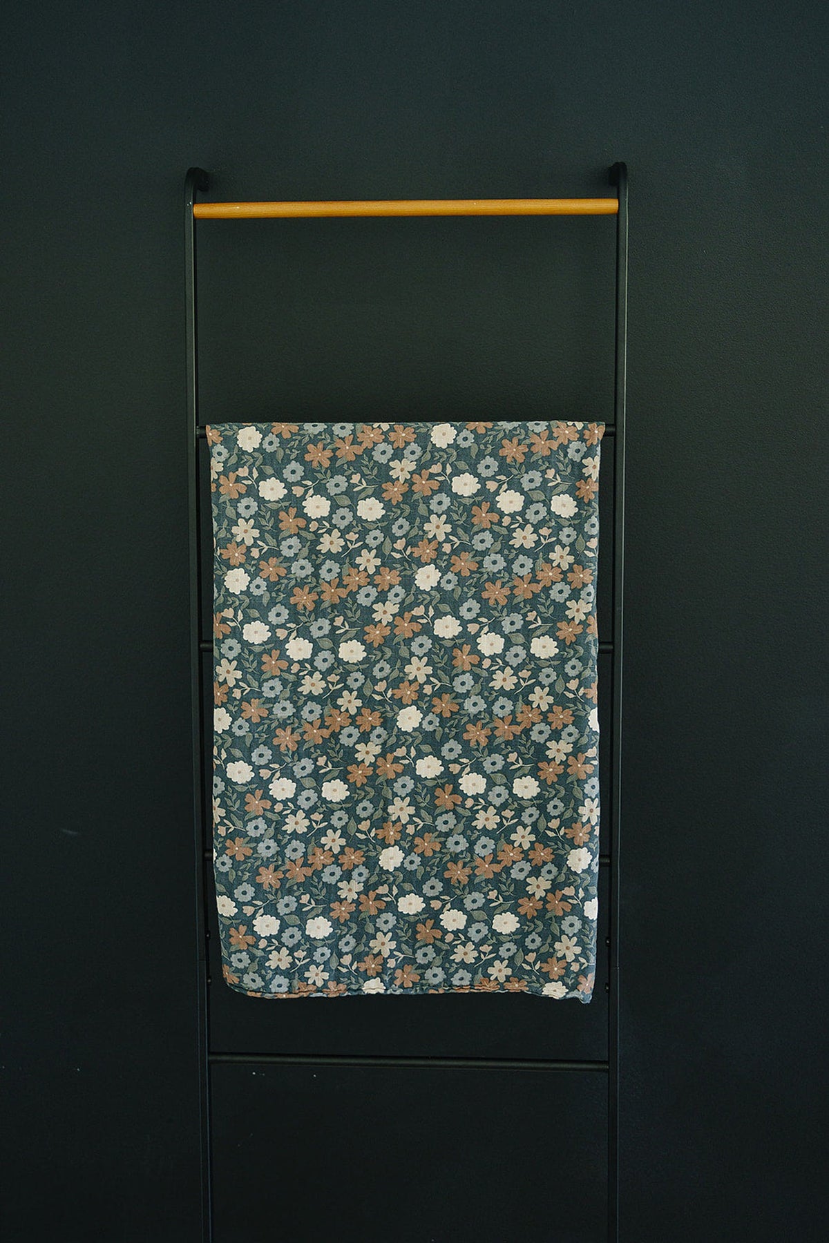 A floral muslin swaddle blanket with blue, white, and brown flowers hangs on a black metal rack.