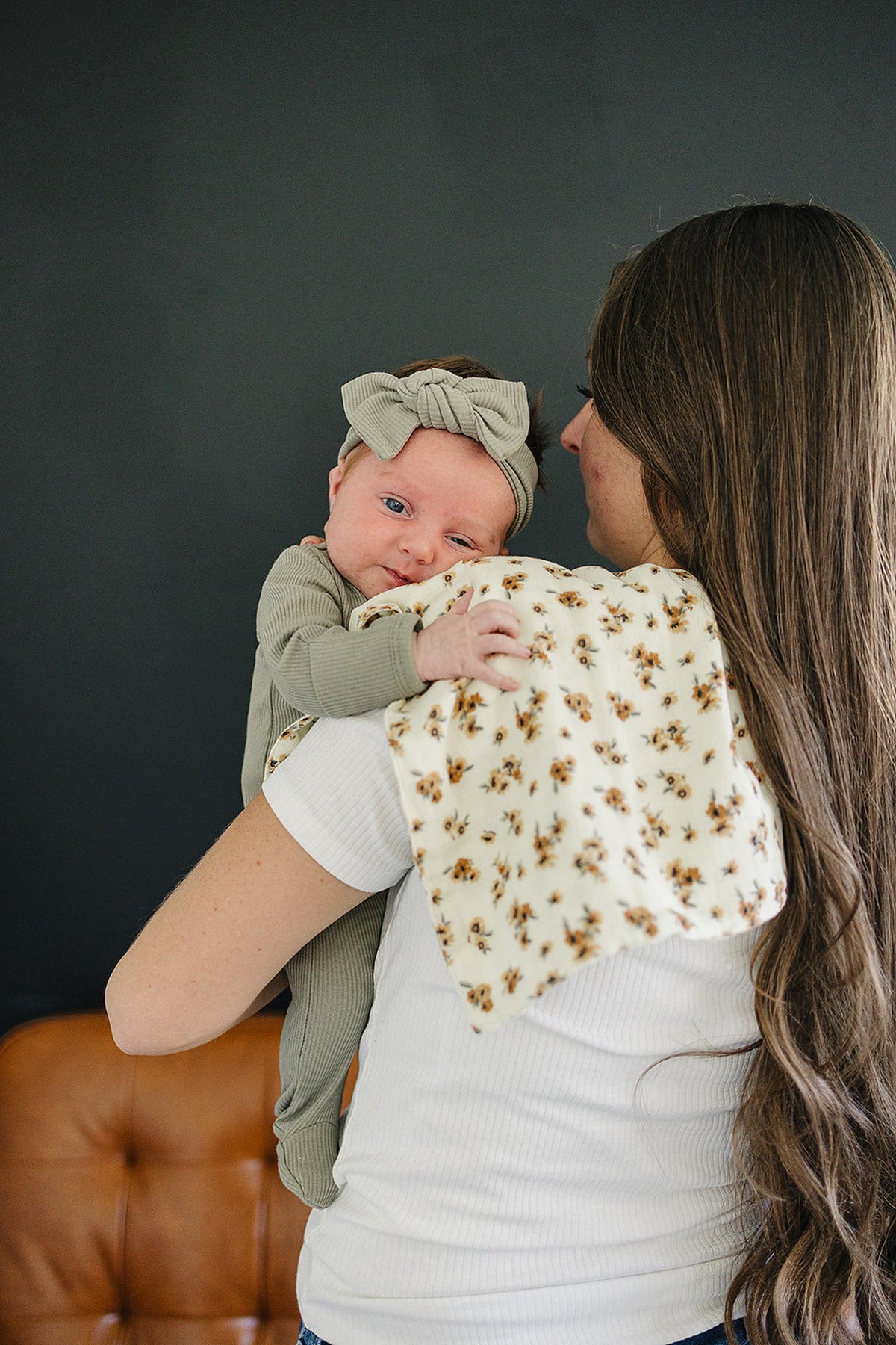 A baby wearing a green outfit and headband rests on a womans shoulder with a floral burp cloth.