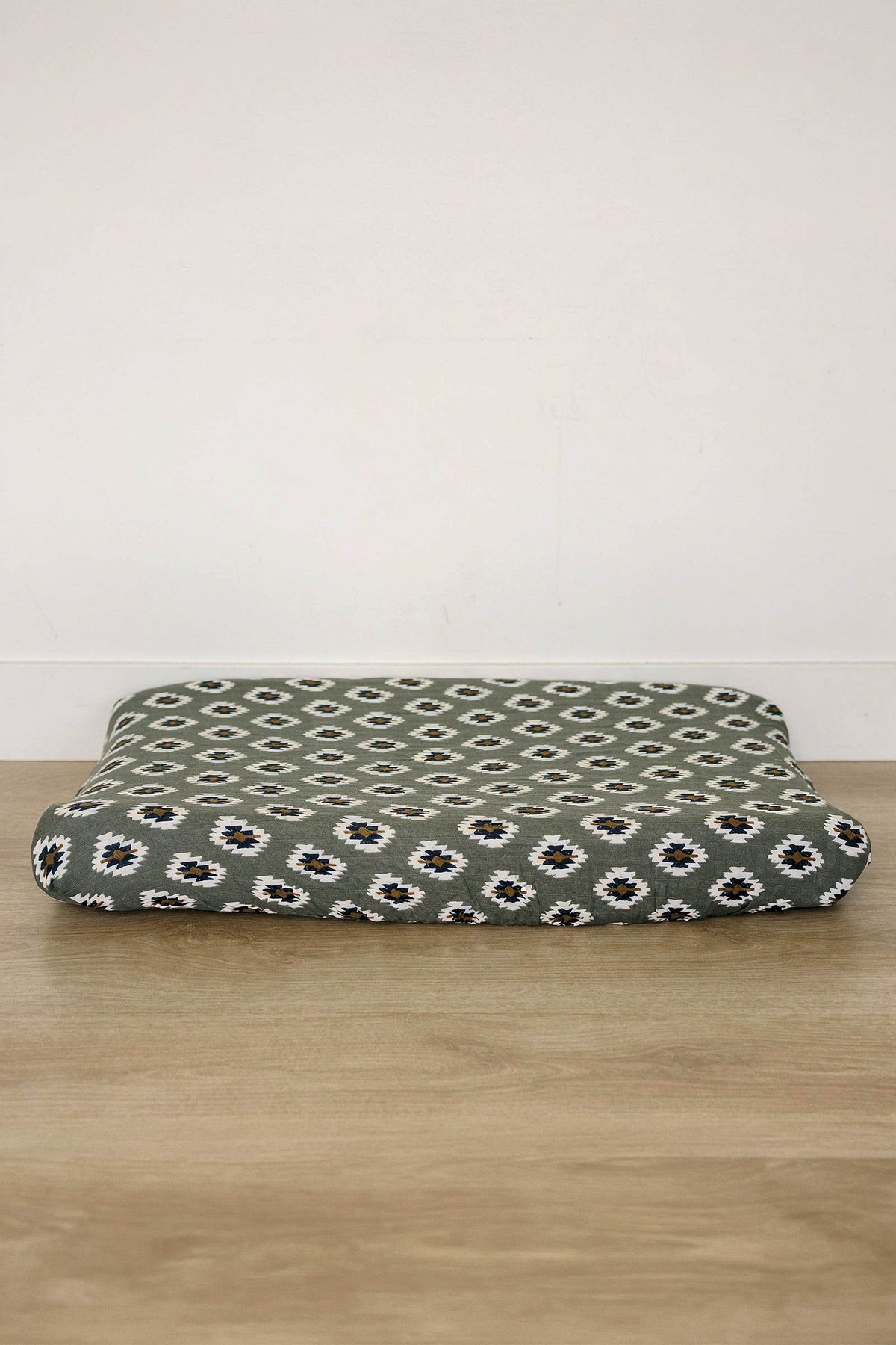A soft, muslin changing pad cover features a Southwest Aztec pattern in green, black, and white. Its breathable fabric is ideal for creating a cozy changing surface.
