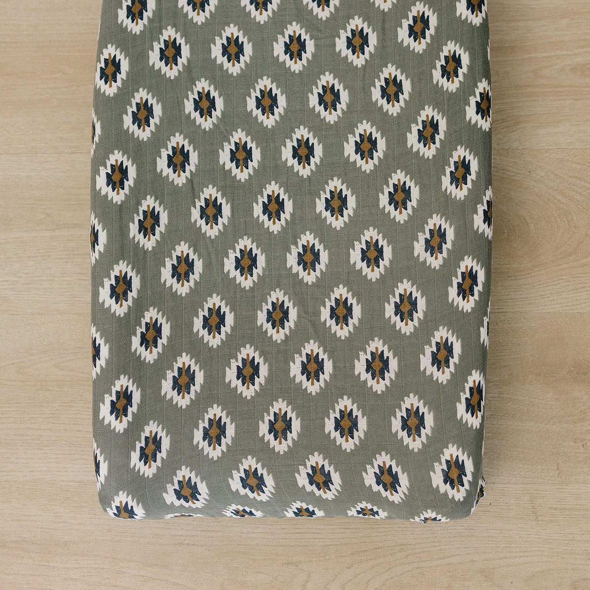Southwest Aztec muslin changing pad cover in a muted green shade features a geometric pattern in cream.