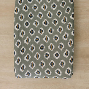 Southwest Aztec muslin changing pad cover in a muted green shade features a geometric pattern in cream.
