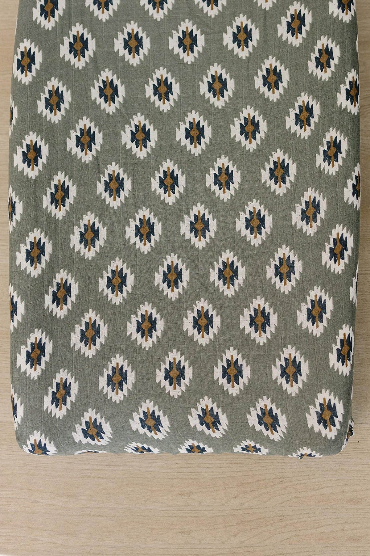 Soft muslin changing pad cover featuring a Southwest Aztec pattern in earthy tones of green, white, and navy. Ideal for adding a cozy, modern touch to any nursery setting.