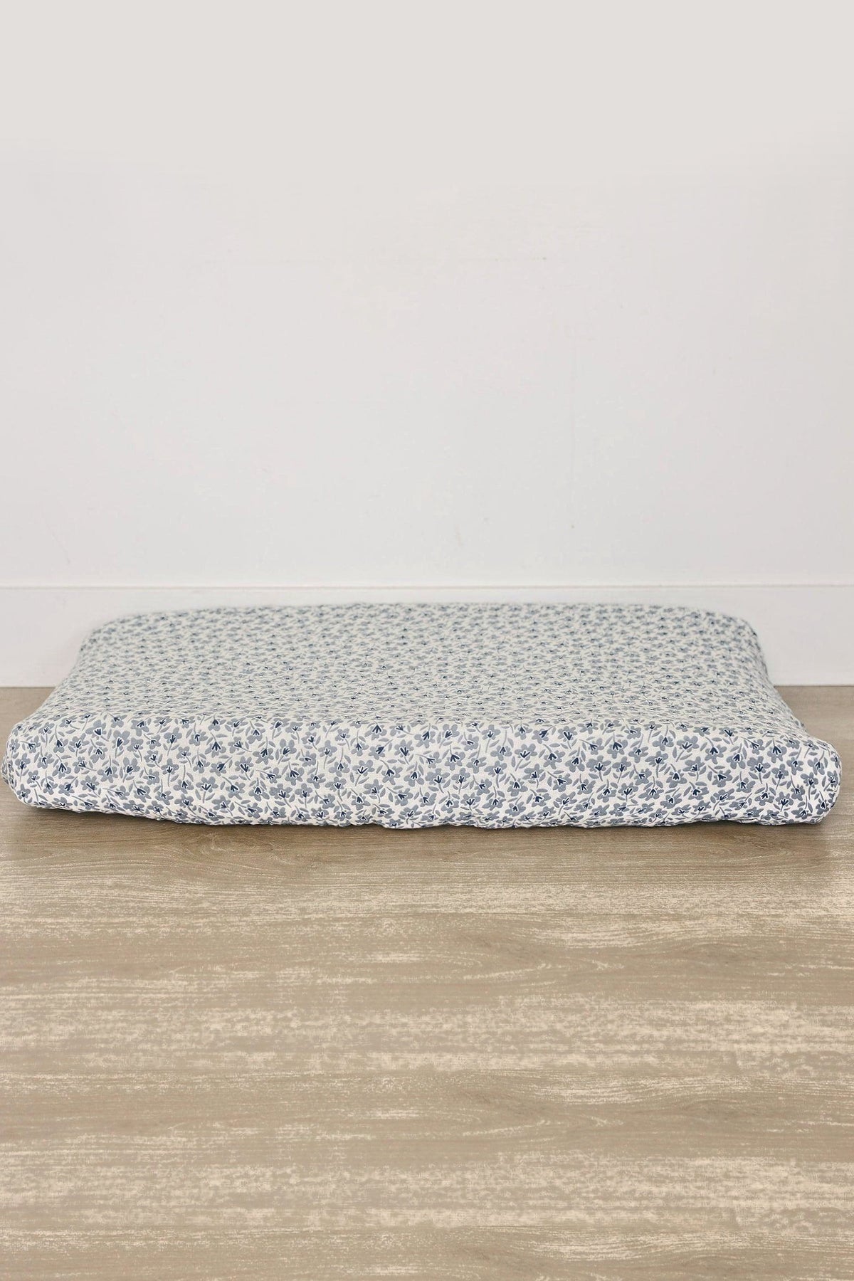 A muslin changing pad cover features a blue floral pattern on a white background, showcasing soft, breathable cotton fabric.
