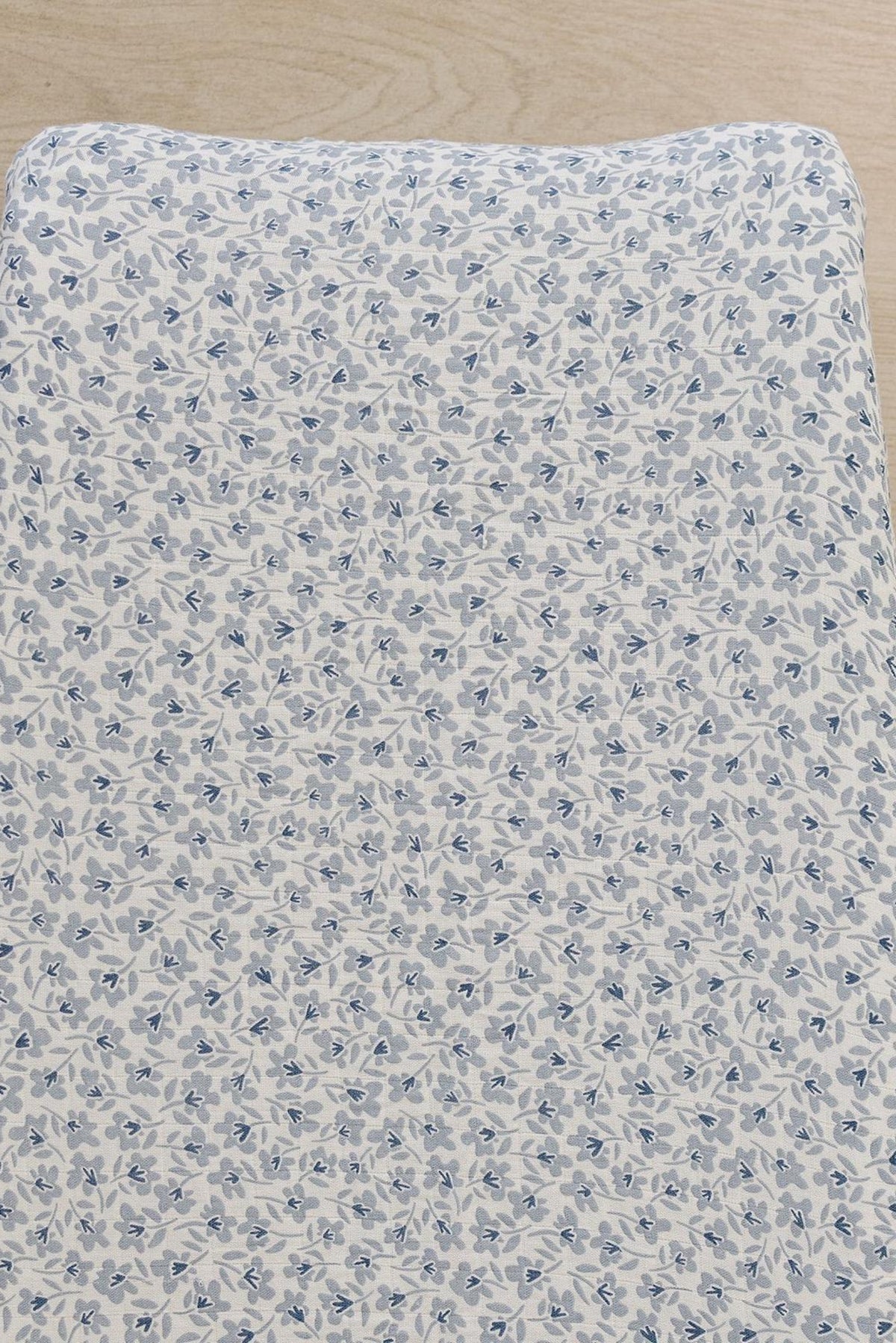 A close-up view of a muslin changing pad cover featuring a delicate blue floral pattern on a light background.