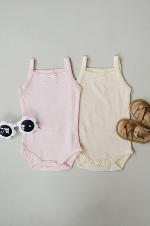 Two baby tank bodysuits in pink and cream, featuring delicate pointelle knit, accompanied by white flower-shaped sunglasses and brown sandals.