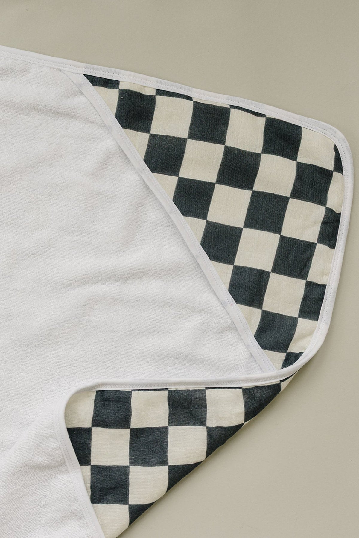 White hooded towel with a charcoal checkered muslin lining, designed for babies, displayed on a neutral background.