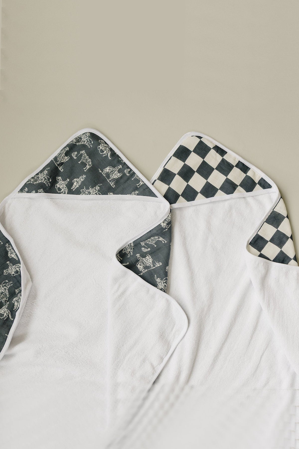 Two white hooded towels with patterned interiors; one has a cowboy print, the other a black and white checkered design.
