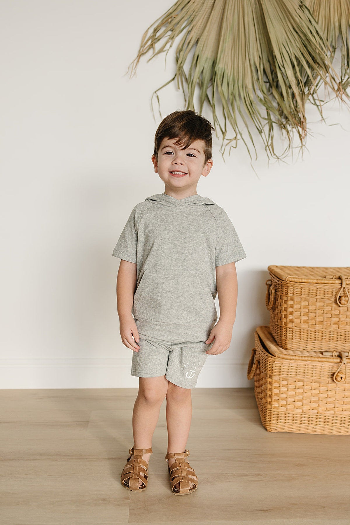 A smiling boy stands in a heather grey hooded t-shirt and matching shorts, showcasing a casual, comfortable style.