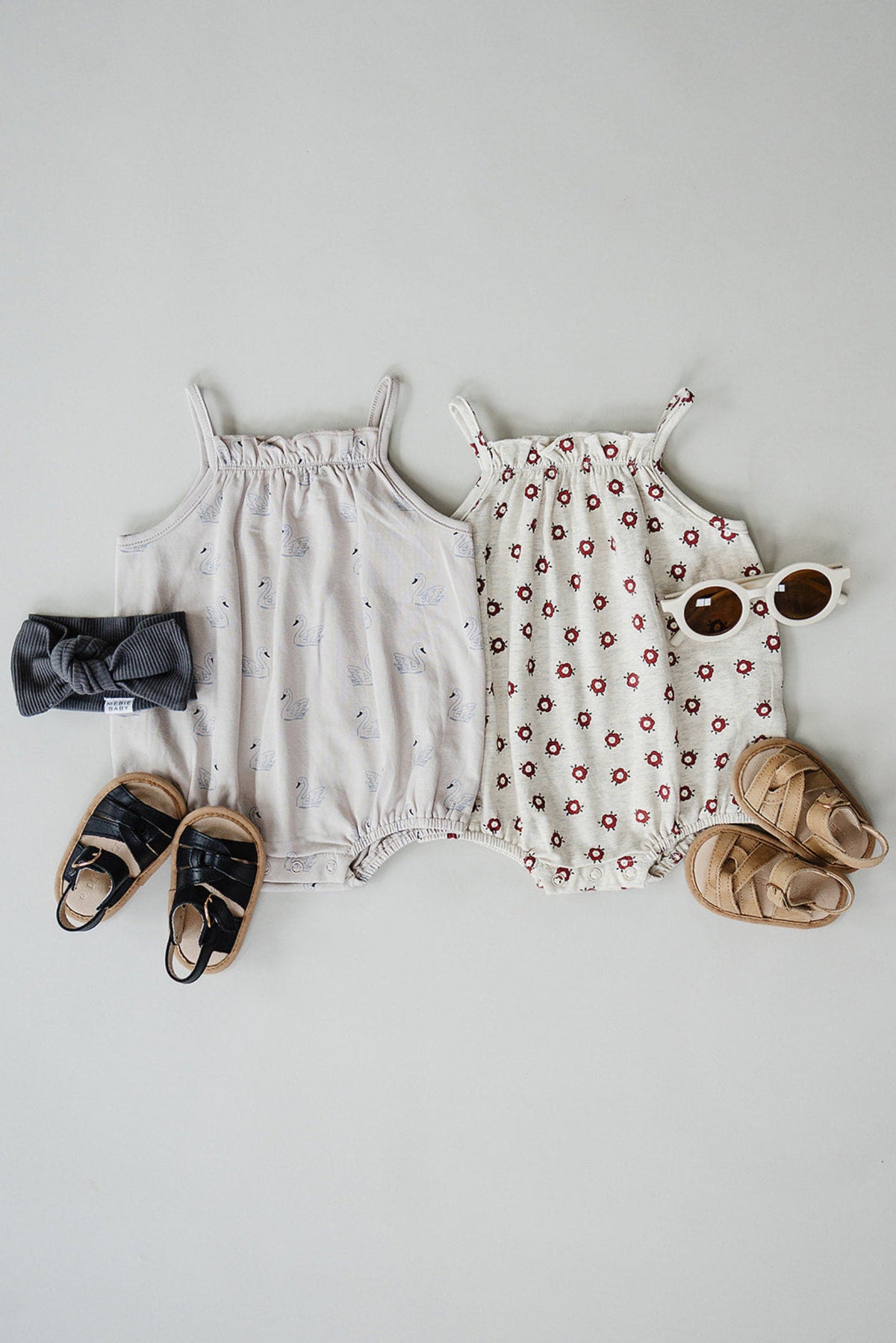 Two baby bubble rompers in soft cotton, one cream with floral prints and the other gray with swan designs, displayed.