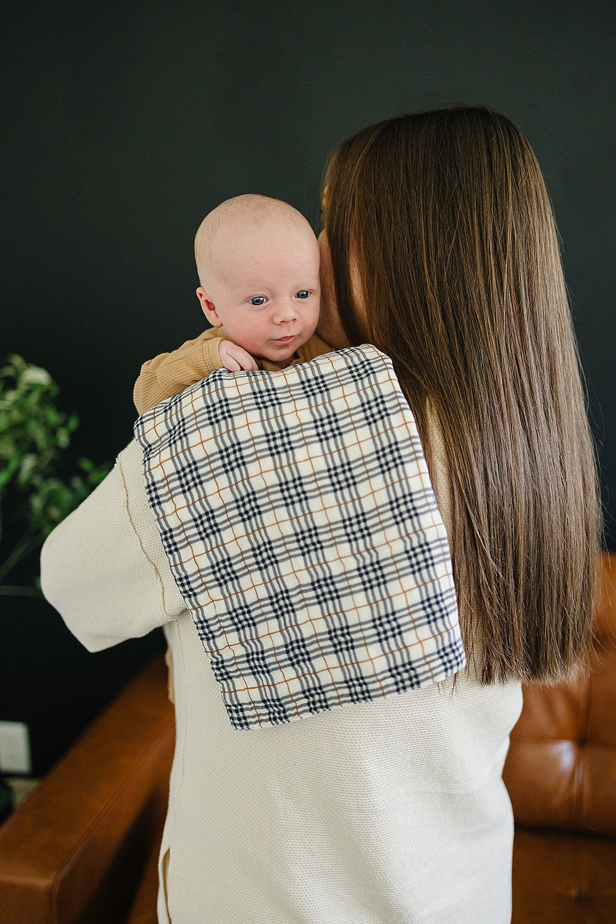 A baby rests on a womans shoulder with a plaid muslin burp cloth draped over her back.
