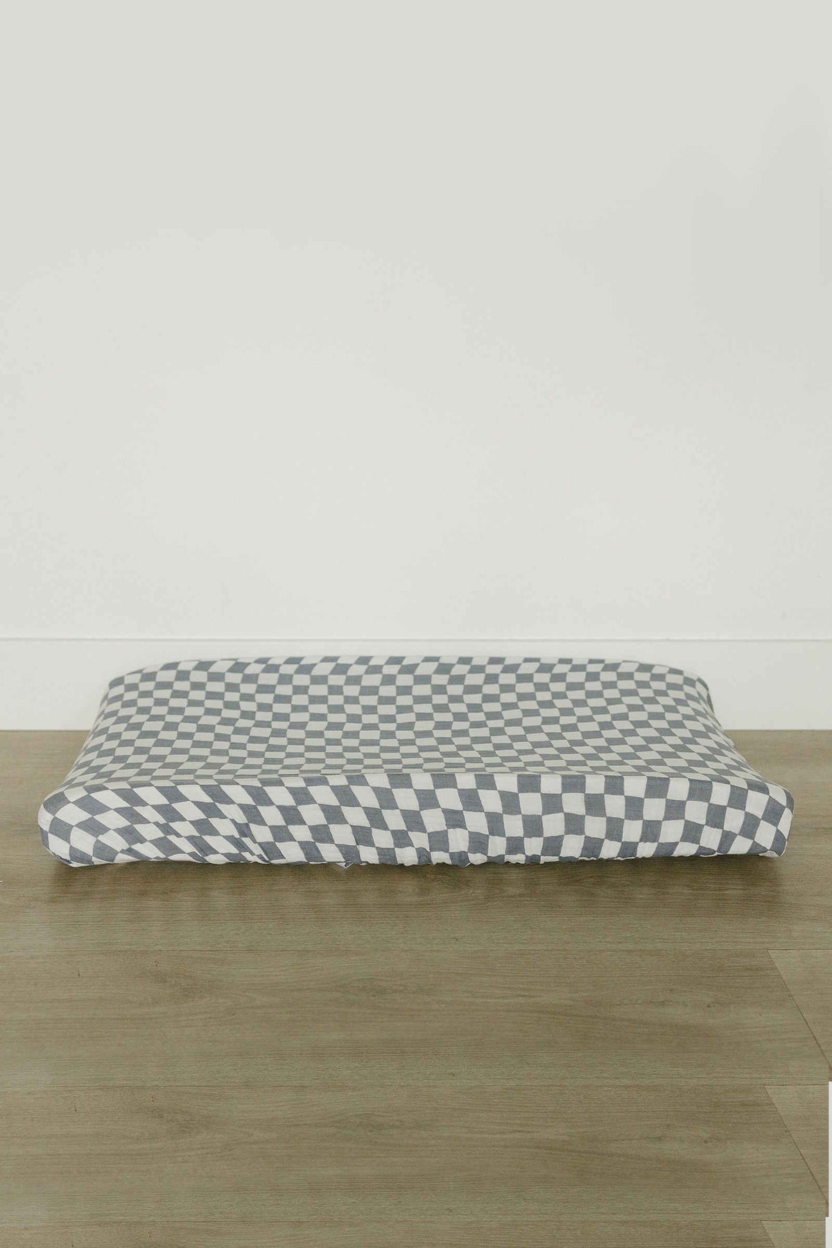 Dusty blue and white wavy checkered muslin changing pad cover on a wooden surface, featuring elasticized edges.